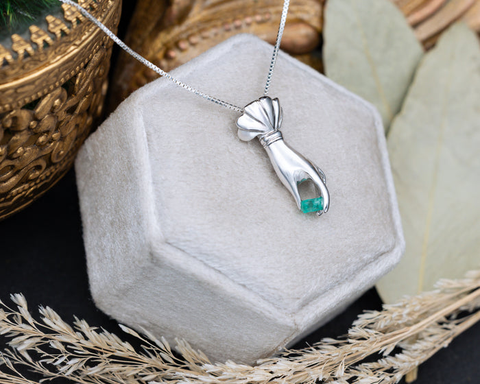 Silver hand pendant with a raw emerald in a hexagonal jewelry box.