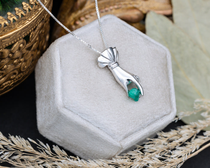 Silver hand pendant with a raw emerald in a hexagonal jewelry box.