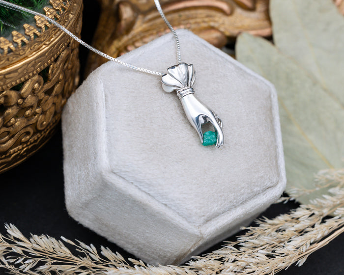Silver hand pendant with a raw emerald in a hexagonal jewelry box.