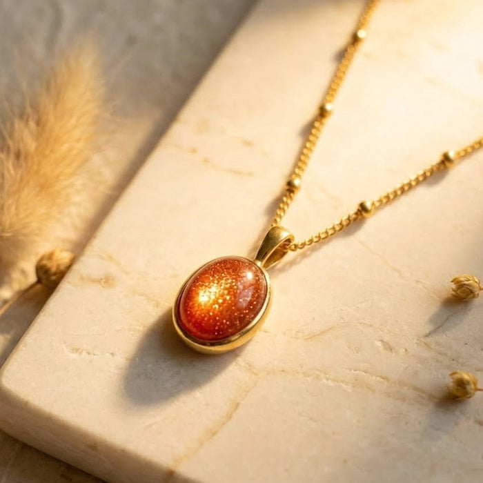 Sunstone necklace displayed on a warm stone surface, featuring an oval orange gemstone pendant in a gold bezel setting on a delicate gold chain.