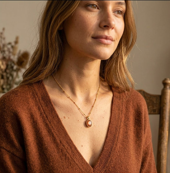 Model wearing a sunstone necklace with a rust sweater, featuring a warm orange oval gemstone pendant on a delicate gold chain.