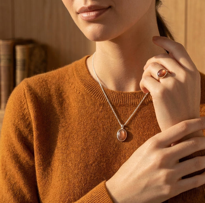 Model wearing a sunstone necklace with a rust-colored sweater, showing the dainty pendant length and warm gemstone tone.