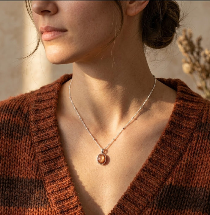 Model wearing a sunstone necklace with a rust sweater, showing a delicate orange gemstone pendant in a gold setting for everyday styling.