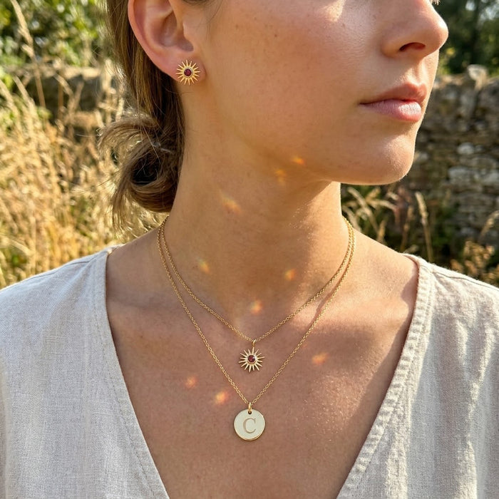 Model wearing a tiny birthstone necklace layered with a small disc pendant, showing minimalist everyday necklace styling.