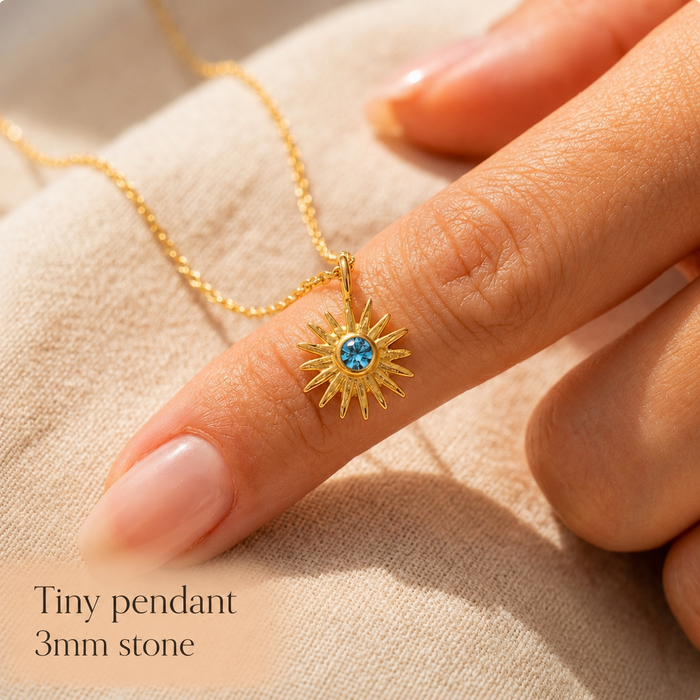 Close-up of a tiny 3mm birthstone pendant on a gold chain beside a finger for scale, showing the petite size of the gemstone necklace.