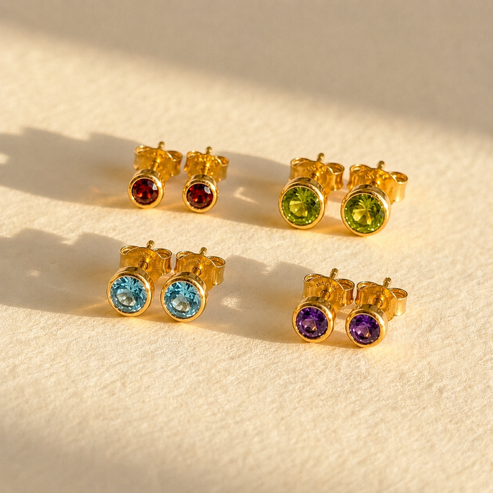 Tiny birthstone stud earrings in gold with colorful gemstones in 3mm and 5mm sizes on soft neutral fabric