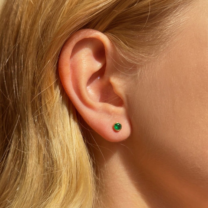 Green birthstone stud earring worn on the ear showing tiny minimalist gemstone size for everyday wear