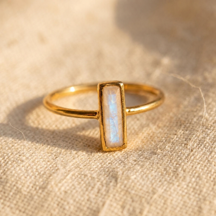 Tiny moonstone bar ring in yellow gold with 10 x 3mm baguette gemstone on linen.