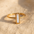 Tiny moonstone bar ring in yellow gold with 10 x 3mm baguette gemstone on linen.