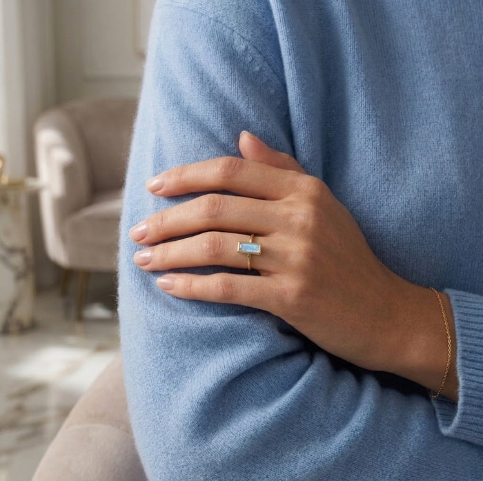 Model wearing moonstone ring with soft blue sweater and delicate everyday styling.
