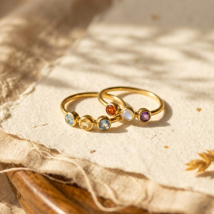 Dainty faceted triple birthstone ring for mom on beige fabric, personalized family ring in gold