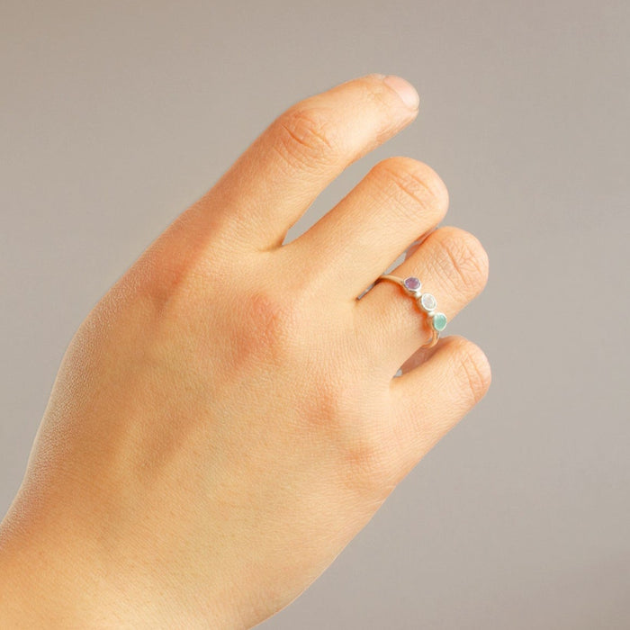 Close-up of woman’s hand wearing a personalized triple birthstone ring with colorful gemstones. A minimalist and elegant stacking ring for mothers, symbolizing children’s birth months — a thoughtful Mother’s Day or family keepsake gift handcrafted in sterling silver, gold, or rose gold.