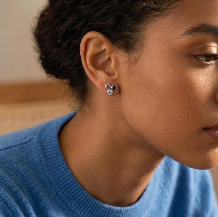 Custom three birthstone stud earrings worn on ear, available in sterling silver, yellow gold vermeil, or rose gold vermeil.