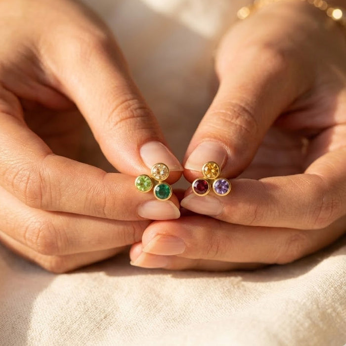 Personalized birthstone stud earrings held between fingers, showing tiny 3mm gemstones in a dainty cluster design.