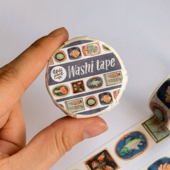 Hand holding a roll of washi tape with decorative designs on a white background