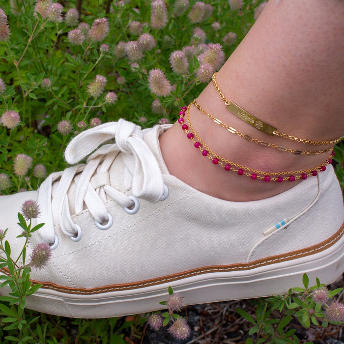 Model is stylishly layering multiple anklets from our collection including the gold filled wire wrapped ruby anklet, gold chain anklet and paw print bar anklet from our pet lovers collection.