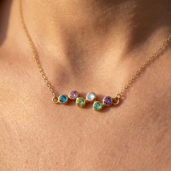 Minimalist mom birthstone necklace featuring a curved zigzag row of bezel-set gemstones, shown in a dainty yellow gold finish.